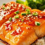 Honey garlic glazed salmon fillets with sesame seeds and green onions on a white plate