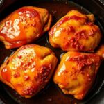 Crispy golden chicken thighs in a cast iron skillet drizzled with hot honey glaze